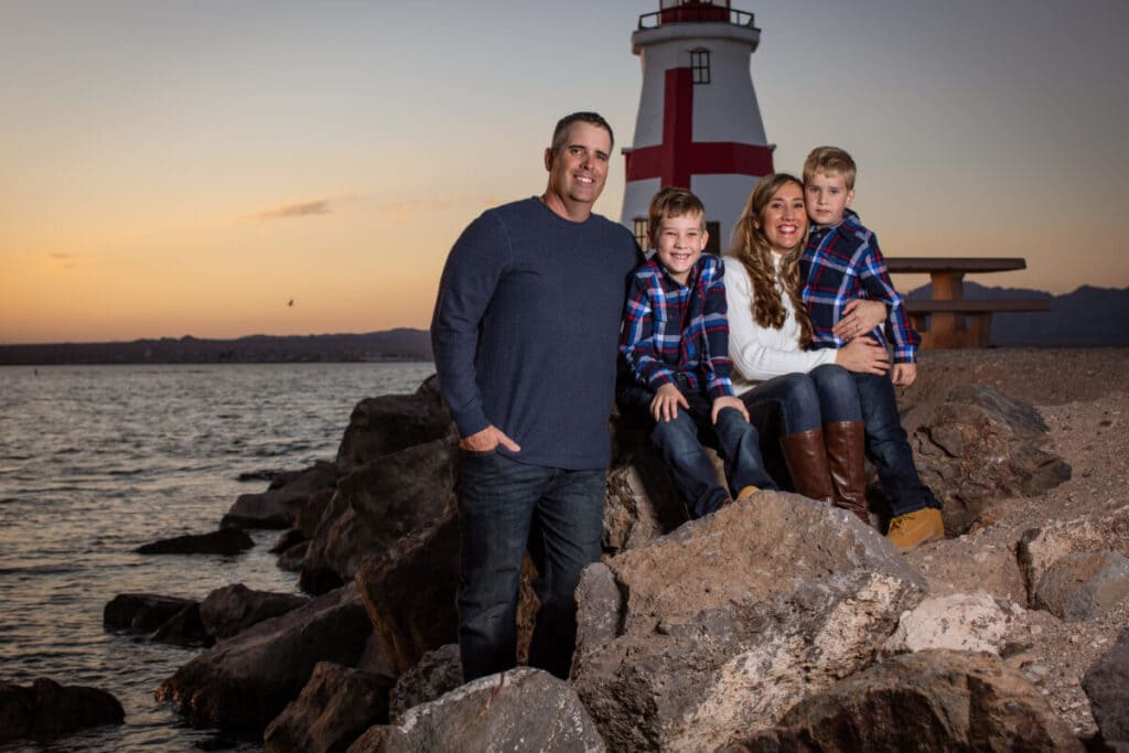 Family photo with rocks and lighthouse by lake at sunset